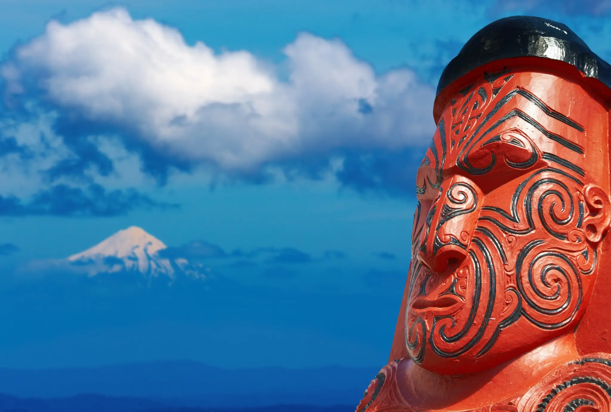 Detalle de una talla maorí con las montañas de Nueva Zelanda al fondo