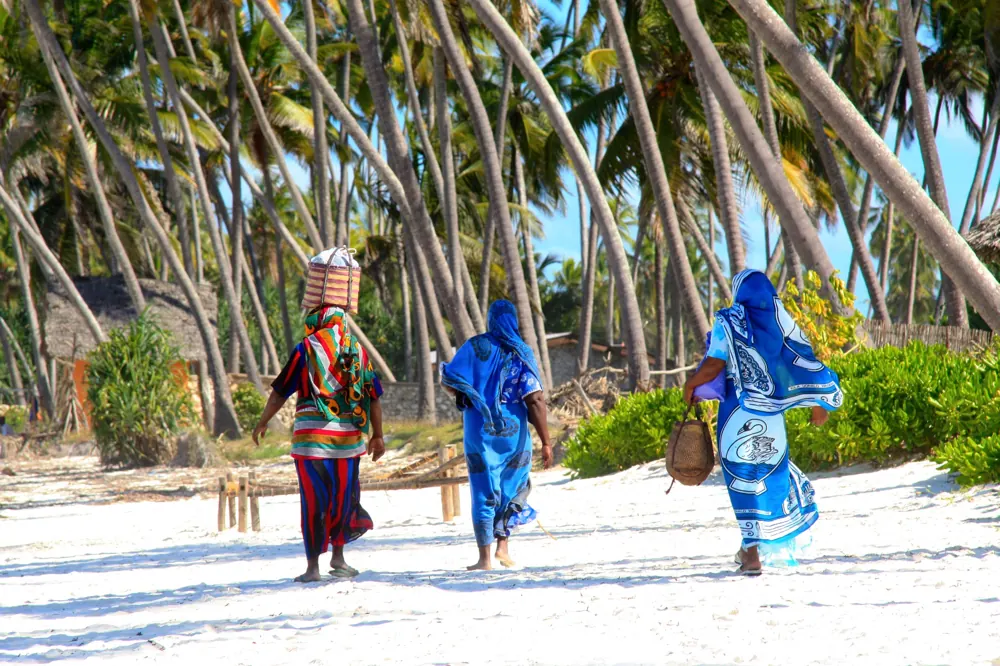 Tres mujeres caminando entre palmeras sobre la arena de Zanzíbar