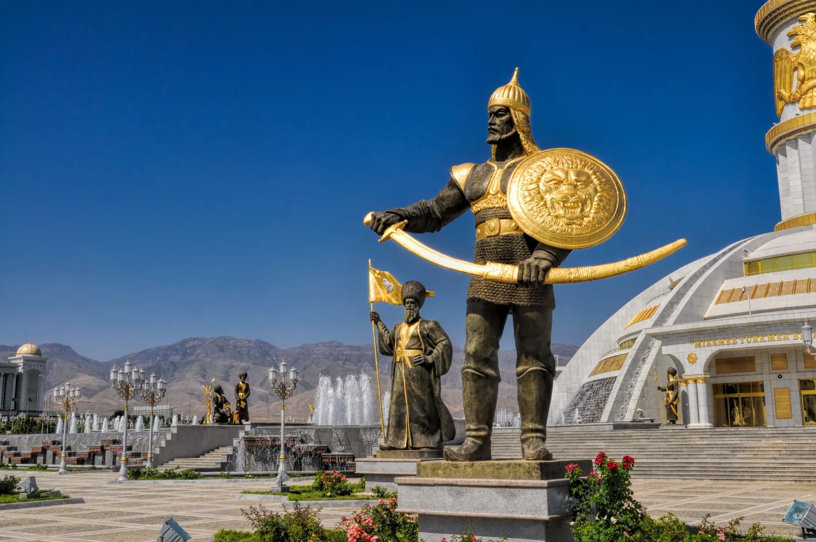 Estatuas doradas con espada y escudo ante edificios monumentales de Asjabad, Turkmenistán